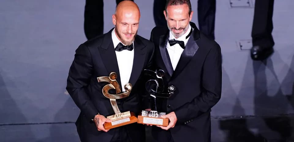 Dos hombres en traje sosteniendo trofeos en evento