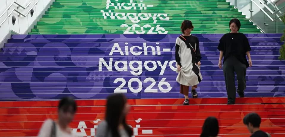 Escalera decorada con Aichi-Nagoya 2026 y personas caminando
