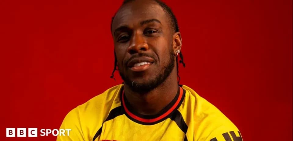 Jugador posando en camiseta de Watford con fondo rojo