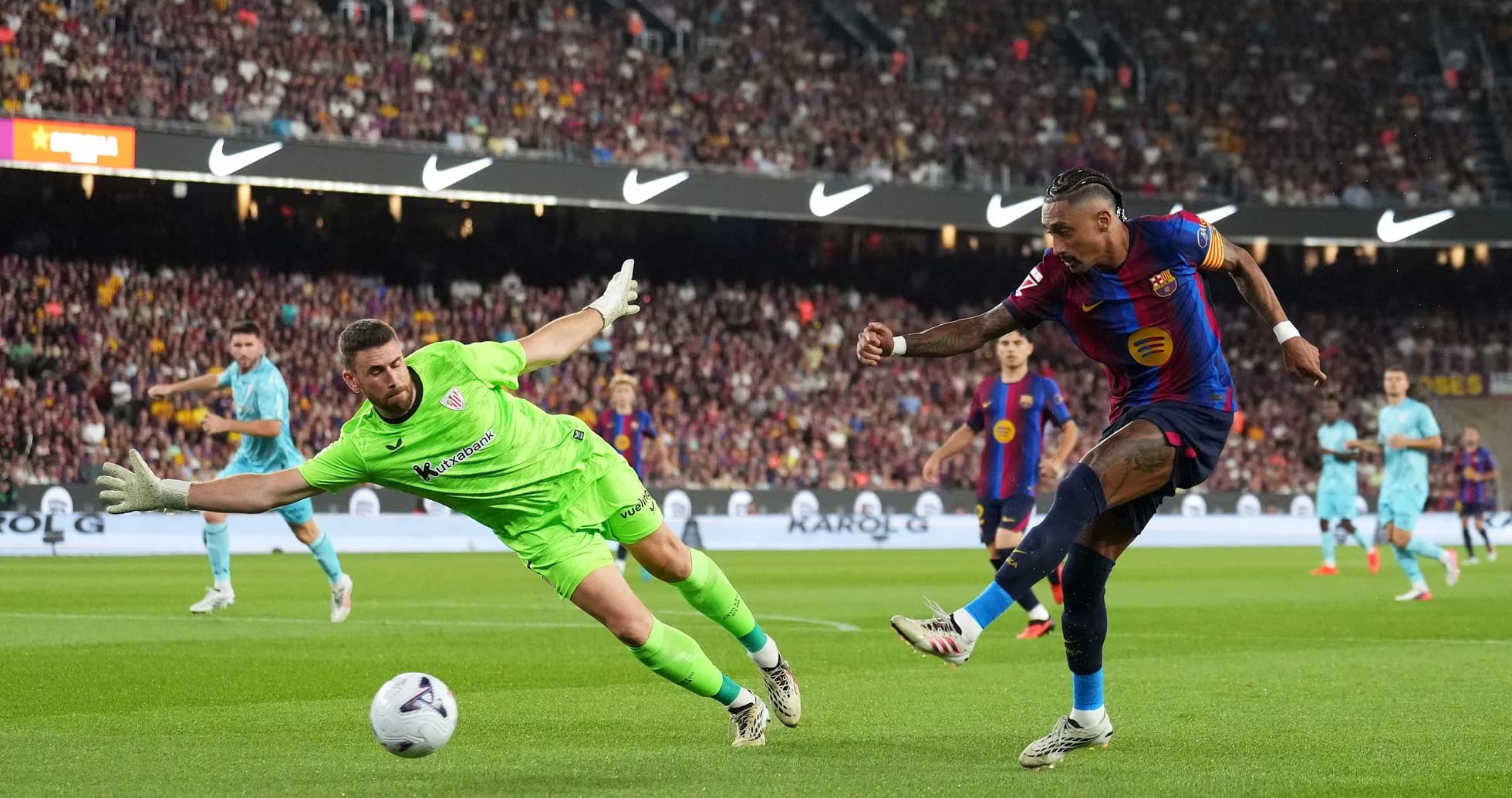 Jugador de Barcelona disparando mientras el portero intenta detenerlo
